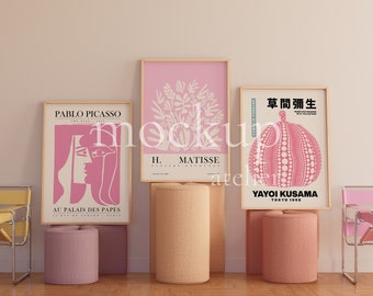 Op de afbeelding: Drie ingelijste kunstprints met roze achtergronden en witte ontwerpen. De prints staan op een plank met twee roze en één beige cilindrische standaards. De prints tonen de namen Pablo Picasso, H. Matisse en Yayoi Kusama. De print van Yayoi Kusama toont de Japanse tekst "草間彌生" en de woorden "Yayoi Kusama" en "Tokyo 1998".