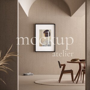 May include: A framed print of a woman with short dark hair, hanging on a beige wall in a modern living room. The room features a round wooden table with chairs, a rug, and a lamp.