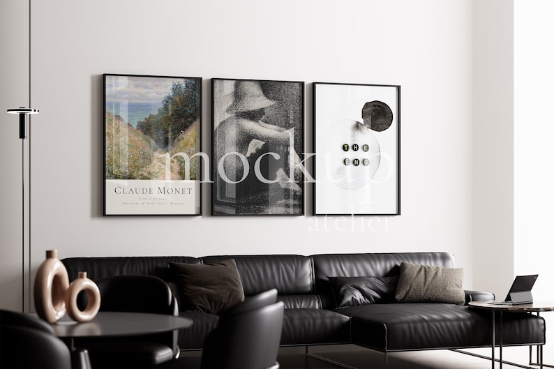 May include: Three framed art prints hanging on a white wall above a black leather sectional sofa. The left print features a landscape painting by Claude Monet. The middle print is a black and white photo of a person wearing a hat. The right print is a black and white abstract design with the text "THE END" in black.
