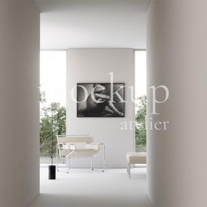 May include: A white chair with a chrome frame sits in a minimalist room with a black and white photograph hanging on the wall. The room has a white floor and white walls.