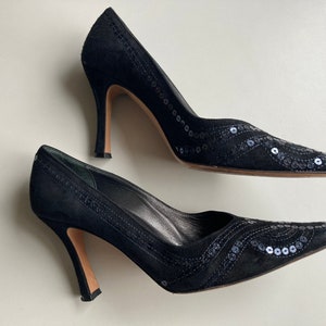 Könnte beinhalten: Ein Paar schwarze Pumps aus Wildleder mit Paillettenbesatz. Die Schuhe haben eine spitze Zehenpartie und einen hohen Stiletto-Absatz.