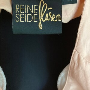 May include: A black label with gold text that reads "REINE SEIDE" and a gold logo. The label also has a white size tag that reads "42".