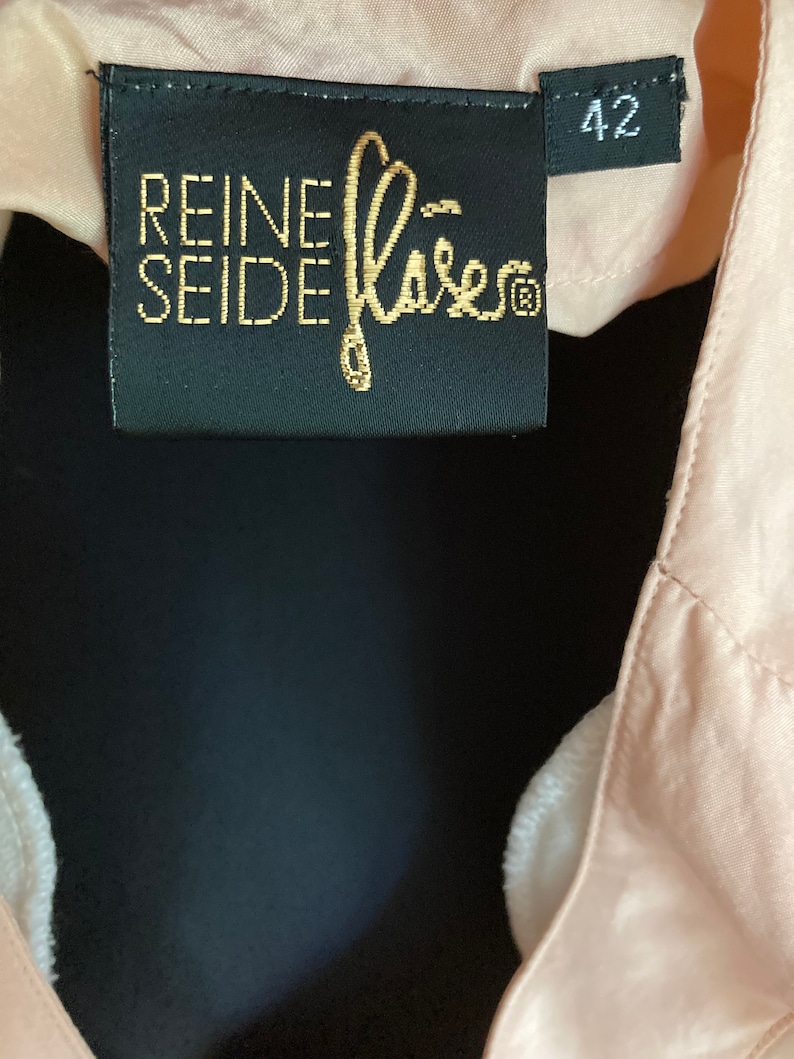 May include: A black label with gold text that reads "REINE SEIDE" and a gold logo. The label also has a white size tag that reads "42".