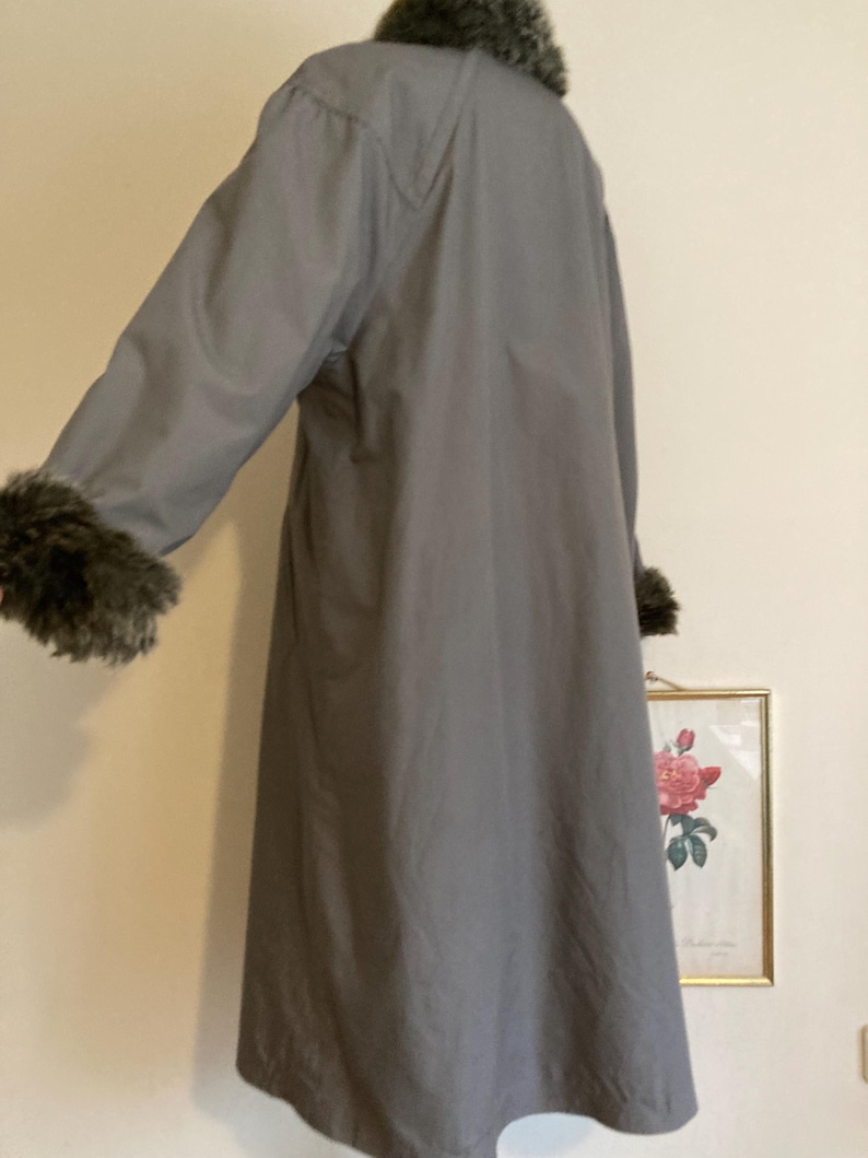 May include: A long gray coat with a faux fur collar and cuffs. The coat has a simple design and is made of a smooth fabric.