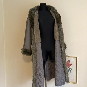 May include: A long, gray faux fur coat with a quilted lining. The coat has a fur collar and cuffs.