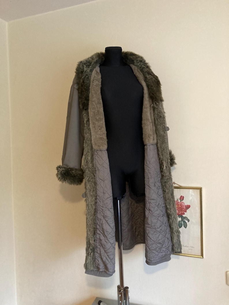 May include: A long, gray faux fur coat with a quilted lining. The coat has a fur collar and cuffs.