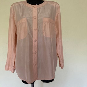 May include: A pale pink, long-sleeved button-up shirt with two patch pockets on the front. The shirt is made of a silky material.