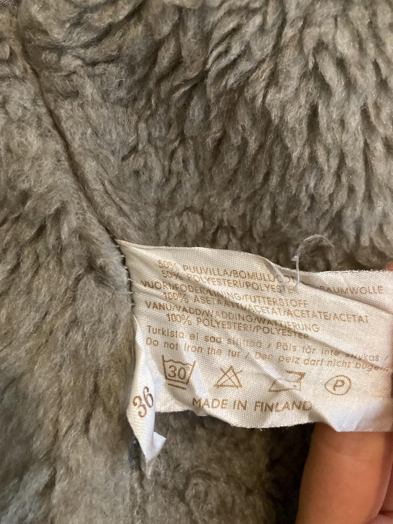 May include: A white tag with black text and symbols. The tag says "50% PUUVILLA/BOMULLUCO 50% POLYESTER/POLYESTER BAUMWOLLE 1VUORDEODER LINING/FUTTERSTOFF 100% ASETAATTACETAT/ACETATE/ACETAT VANU/VADD/WADDING/WANTIERUNG 100% POLYESTERI/POLYESTER Turkista el saa sit&auml;&auml; Pals f&ouml;r intewukas/ Do not fron the fur/ Der peiz dari nicht buge 36 30 MADE IN FINLAND P"
