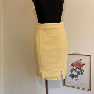 Può includere: Una gonna di colore giallo pallido con una silhouette dritta e aderente. La gonna ha un'alta vita e una leggera fessura su ciascun lato. La gonna è realizzata in un tessuto liscio e testurizzato.