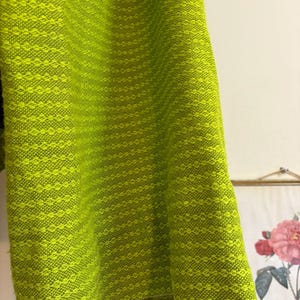 May include: Close-up of a vibrant, chartreuse-colored fabric with a textured, diamond-like pattern. The fabric appears to be a woven material, possibly for clothing or home decor. The bright green color dominates the image.