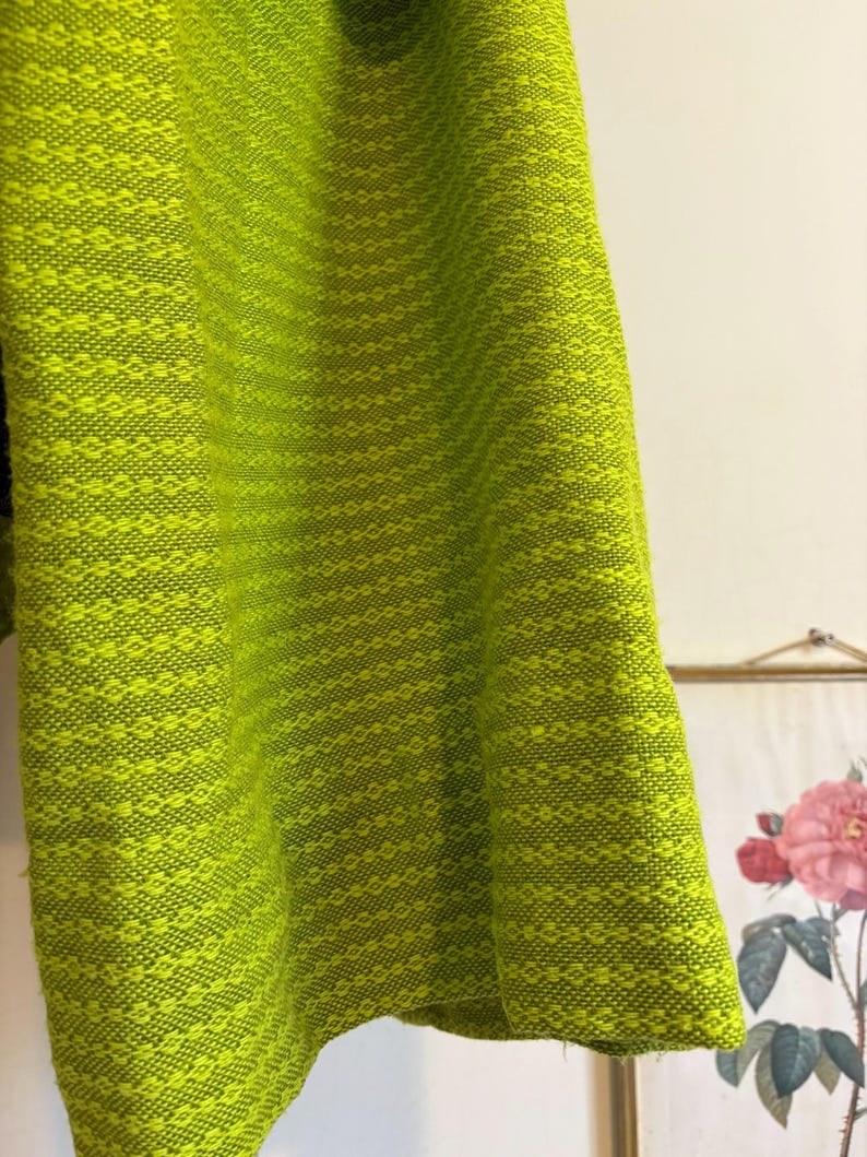 May include: Close-up of a vibrant, chartreuse-colored fabric with a textured, diamond-like pattern. The fabric appears to be a woven material, possibly for clothing or home decor. The bright green color dominates the image.