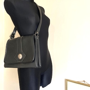 Pode incluir: Bolsa de ombro preta com fecho de aba e fecho prateado. A bolsa tem formato retangular com uma al&ccedil;a longa. A bolsa &eacute; exibida em um manequim preto.