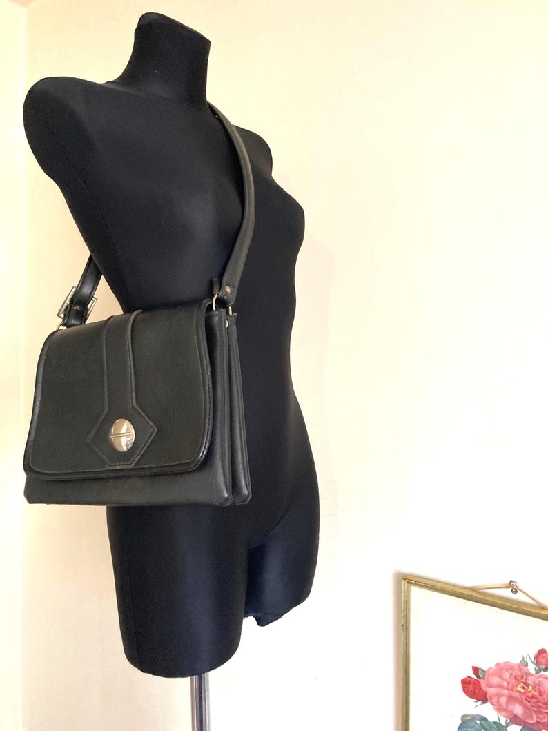 Pode incluir: Bolsa de ombro preta com fecho de aba e fecho prateado. A bolsa tem formato retangular com uma al&ccedil;a longa. A bolsa &eacute; exibida em um manequim preto.