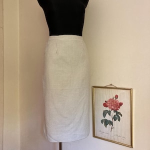 Peut inclure: Une jupe crayon en gingham blanc et gris sur un mannequin. La jupe est au niveau du genou et a une silhouette droite.