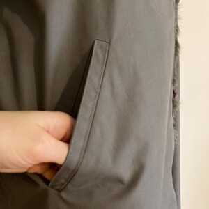 May include: A gray, long,  faux fur-trimmed vest with a large pocket on the left side.
