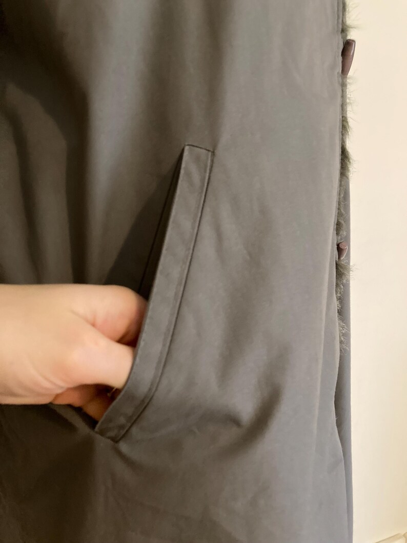 May include: A gray, long,  faux fur-trimmed vest with a large pocket on the left side.