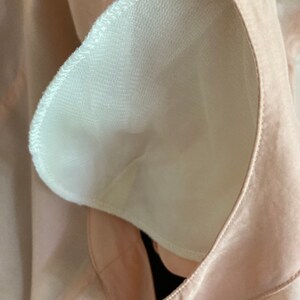 May include: Close-up of a light pink fabric with a white mesh lining. The fabric has a seam around the edge of the mesh lining.