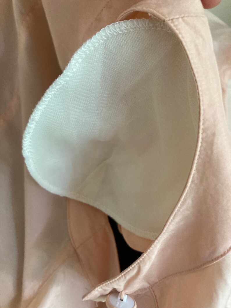 May include: Close-up of a light pink fabric with a white mesh lining. The fabric has a seam around the edge of the mesh lining.