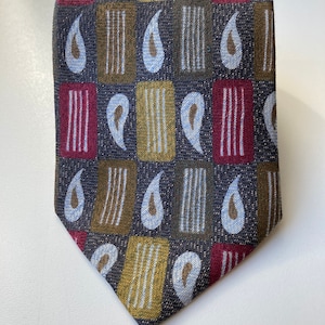 Op de afbeelding: Een donkerbruine stropdas met een geometrisch patroon van blauwe, rode en gouden paisley-vormen en verticale strepen.