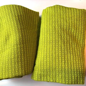 May include: Two folded lime green fabric pieces with a textured, diamond-like pattern. The fabric has a woven appearance and a soft, inviting texture. The items appear to be decorative or functional textiles.