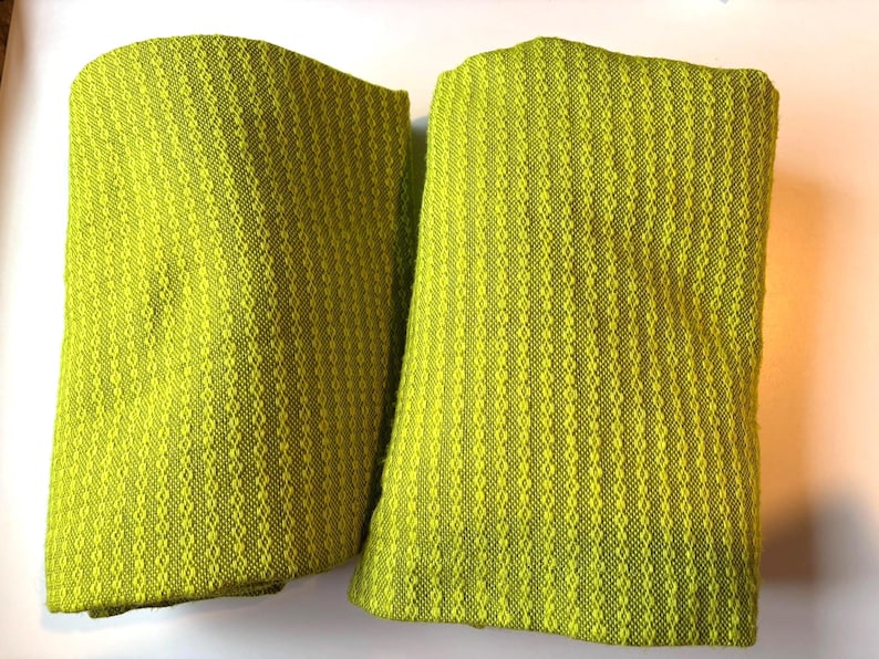 May include: Two folded lime green fabric pieces with a textured, diamond-like pattern. The fabric has a woven appearance and a soft, inviting texture. The items appear to be decorative or functional textiles.