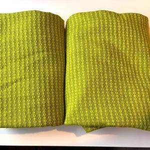May include: Two folded, textured, chartreuse-colored fabric pieces. The fabric has a woven pattern of vertical lines and small diamond shapes. The items are displayed on a white surface.