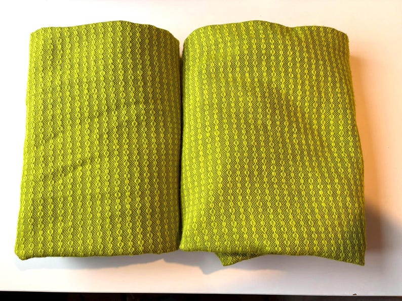 May include: Two folded, textured, chartreuse-colored fabric pieces. The fabric has a woven pattern of vertical lines and small diamond shapes. The items are displayed on a white surface.