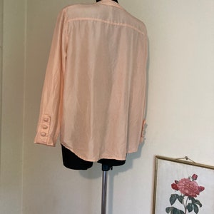 May include: A pale pink long-sleeved button-up shirt with a mandarin collar. The shirt is made of a silky material and has three buttons on each cuff.