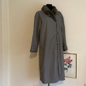 May include: A long, gray coat with a faux fur collar. The coat has a button closure and is on a mannequin.