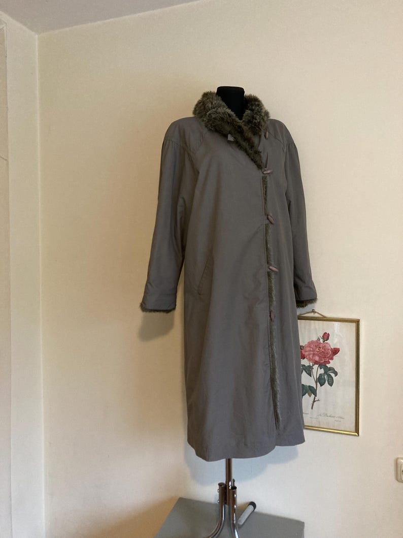 May include: A long, gray coat with a faux fur collar. The coat has a button closure and is on a mannequin.