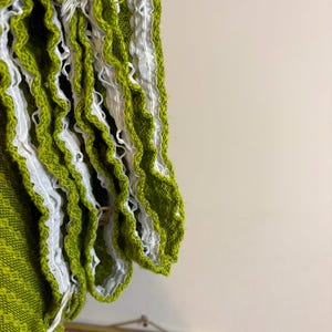 May include: Close-up of a lime green knitted fabric with white ruffled trim. The fabric has a textured appearance and is likely part of a garment. The white trim adds a decorative element to the edge of the fabric.