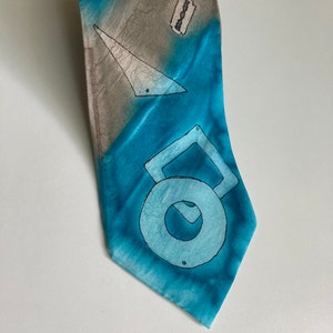 May include: A blue and grey silk tie with a geometric pattern. The pattern includes a triangle, a square, and a circle. The tie is made of a soft, smooth fabric.
