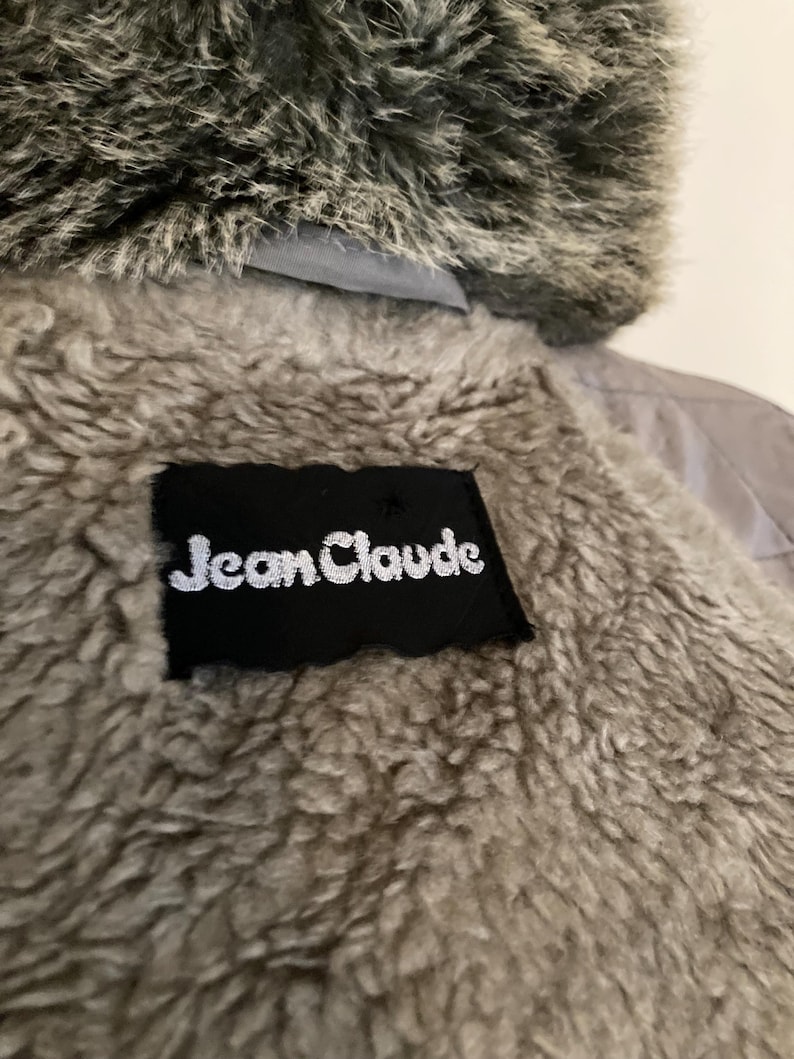 May include: A gray faux fur hooded jacket with a black label that reads "Jean Claude" on the back.