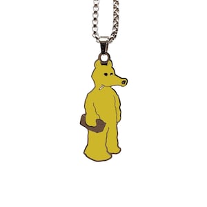 Puede incluir: Collar con colgante amarillo que presenta una figura de dibujos animados con un hocico largo, sosteniendo un maletín y un cigarrillo. El colgante está suspendido de una cadena plateada, creando un accesorio único y llamativo.