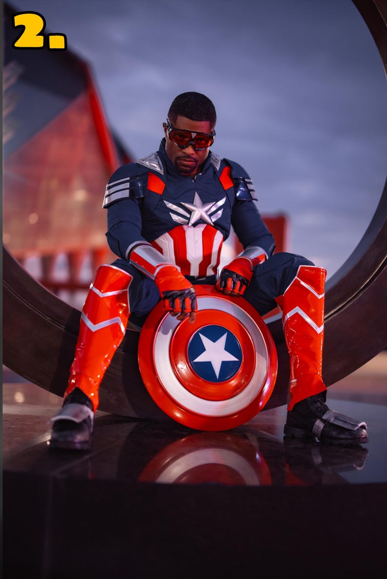 Pode incluir: Uma pessoa com uma fantasia do Capit&atilde;o Am&eacute;rica, vestindo um traje azul marinho e vermelho com uma estrela branca no peito. Eles est&atilde;o segurando um escudo vermelho, branco e azul com uma estrela branca. A pessoa est&aacute; usando botas e luvas vermelhas.