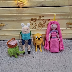 Op de afbeelding: Gehaakte pluche speelgoed van personages uit de animatieserie Adventure Time. De personages zijn Finn de mens, Jake de hond, Prinses Bubblegum en Lumpy Space Princess.