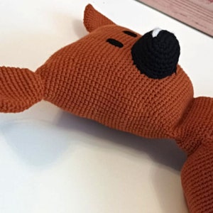 Könnte beinhalten: Ein gehäkeltes Stofftier in Form eines Fuchses mit braunem Körper, schwarzer Nase und weißen Akzenten.