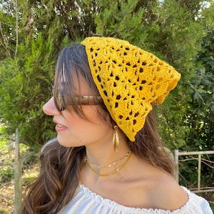 May include: A bright yellow, crocheted headscarf with an openwork floral design. The head covering is worn on the head. The headscarf is made of a soft, textured yarn. The headscarf is a stylish accessory.