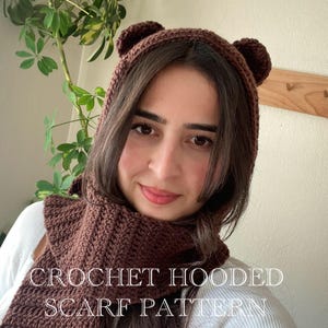 May include: A brown crocheted hooded scarf with bear ears. The scarf is worn by a person with long brown hair. The text "CROCHET HOODED SCARF PATTERN" is visible at the bottom of the image.