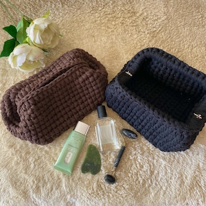 May include: Two crocheted storage baskets, one brown and one black, with a variety of beauty products, including a bottle of lotion, a jade roller, and a gua sha tool.