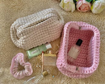 Peut inclure: Deux sacs en crochet, l'un beige et l'autre rose, contenant divers articles de toilette et accessoires. Les sacs sont fabriqués avec un point texturé et présentent un design simple et élégant.