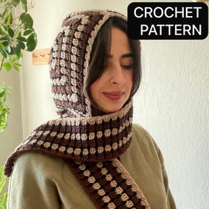 May include: A crocheted hood and scarf set in shades of brown and cream. The hood features a checkered pattern, and the scarf is designed to be worn around the neck. The text "CROCHET PATTERN" is displayed in a black box.