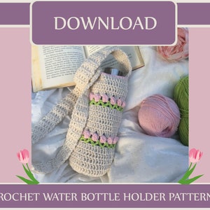 Op de afbeelding: Een haakpatroon voor een waterfleshouder met een witte gehaakte fleshouder met roze en groene accenten. De houder bevindt zich op een wit oppervlak met een boek, garen en bloemen.