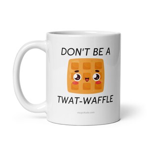 Op de afbeelding: Een witte keramische koffiemok met een zwarte en gele cartoonwafel met een glimlachend gezicht. De tekst op de mok luidt "Don't be a twat-waffle" en "mugs4sale.com".