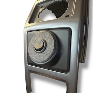 Op de afbeelding: Een close-up van een zwarte schakelaar met een blauwe LED-lamp, gemonteerd in een grijs kunststof paneel.