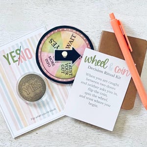 May include: A decision-making kit with a wheel, coin, pen, and notepad. The wheel has sections like "Yes" and "Wait." The coin says "Yes." The notepad and pen are coral. The kit includes a card with instructions.
