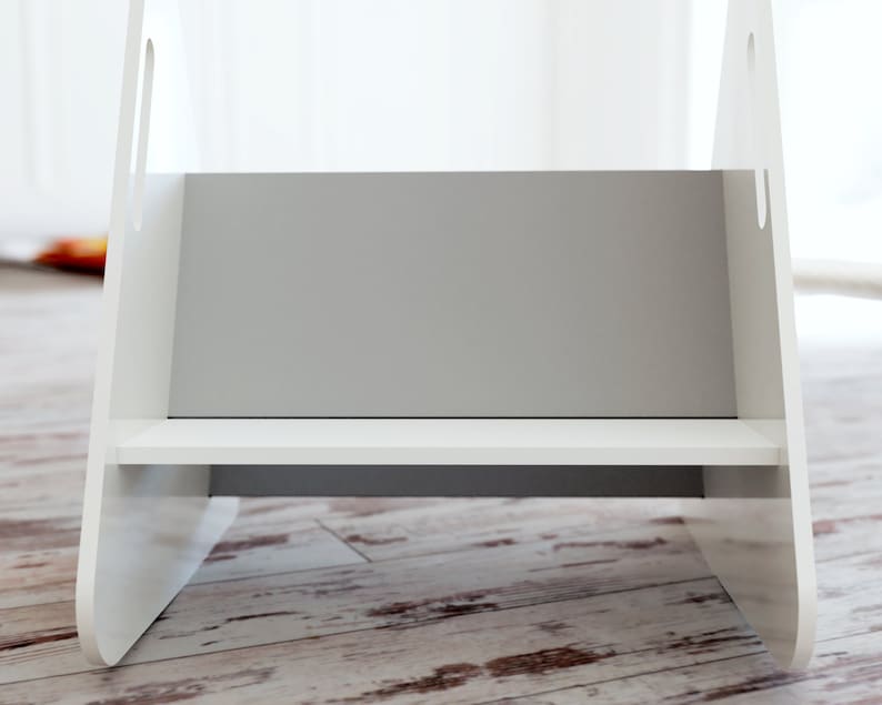 May include: A white wooden step stool with a grey interior and a single shelf. The stool has cut-out handles on the sides and is designed for children or to reach higher places. The step stool is on a wooden floor.