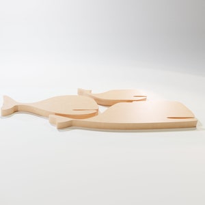 Puede incluir: Tres recortes de ballenas de madera de diferentes tama&ntilde;os. Las ballenas son de madera de color claro y tienen un dise&ntilde;o simple y minimalista. La ballena m&aacute;s grande mide aproximadamente 30 cm de largo, siendo las otras dos m&aacute;s peque&ntilde;as.