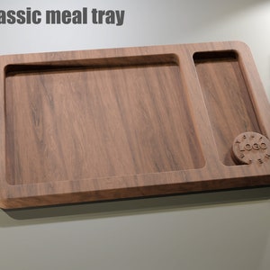 Puede incluir: Una bandeja de comida de madera con una secci&oacute;n principal rectangular y un compartimento m&aacute;s peque&ntilde;o, rectangular. La bandeja tiene un acabado de veta de madera oscura y una hendidura circular con la palabra "LOGO". El texto "Classic meal tray" est&aacute; en la parte superior.