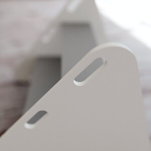 May include: Close-up of two white, triangular wooden storage boxes. Each box has a rounded top with a rectangular cutout. The boxes are positioned at an angle, with one slightly behind the other, creating a sense of depth.